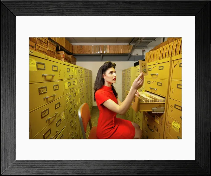 Framed Print : Vintage lifestyle shoot in ClassicStock office. Woman in vintage wardrobe sitting in image archive room going through file cabinets looking at slides and negatives