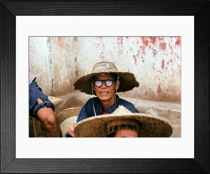 Framed Print : Man wearing a straw hat and black rimmed glasses sitting outside a building Framed Print : Man wearing a straw hat and black rimmed glasses sitting outside a building