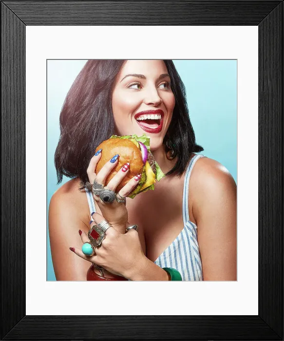 Framed Print : A woman in front of a blue background eating a burger Framed Print : A woman in front of a blue background eating a burger