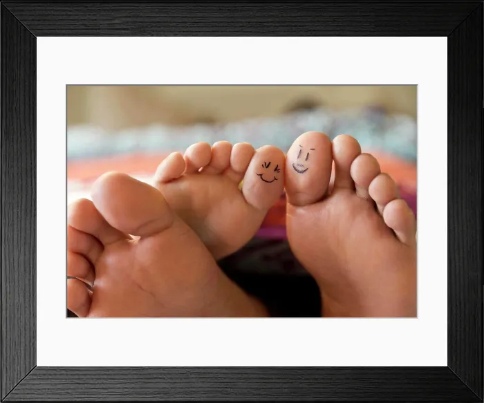 Framed Print : Close-up of bare feet sticking out from covers while couple lays in bed, with smiley faces drawn on big toes Framed Print : Close-up of bare feet sticking out from covers while couple lays in bed, with smiley faces drawn on big toes
