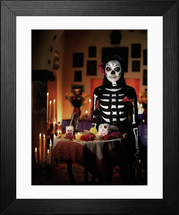Framed Print : Female skeleton with ribbons and a flower in her hair standing behind a Dios de los Muertos altar