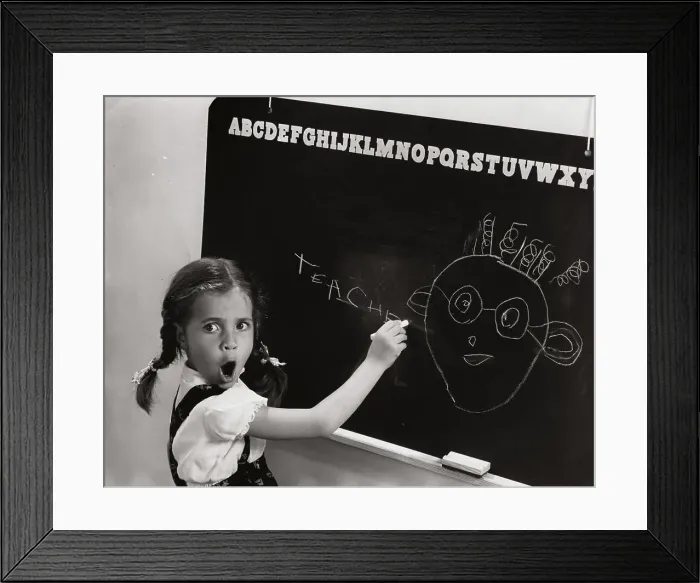 Framed Print : Side profile of a girl drawing a cartoon of her teacher on the blackboard Framed Print : Side profile of a girl drawing a cartoon of her teacher on the blackboard