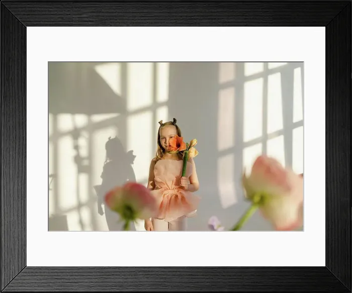 Framed Print : Girl holding flower on face standing in front of white wall Framed Print : Girl holding flower on face standing in front of white wall