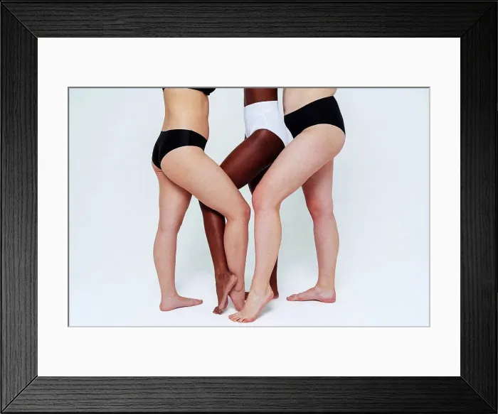Framed Print : Female friends standing with legs crossed at ankle in studio Framed Print : Female friends standing with legs crossed at ankle in studio