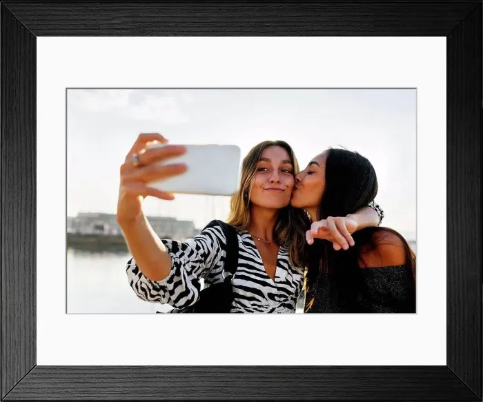 Framed Print : Young woman kissing friend while taking selfie against clear sky Framed Print : Young woman kissing friend while taking selfie against clear sky