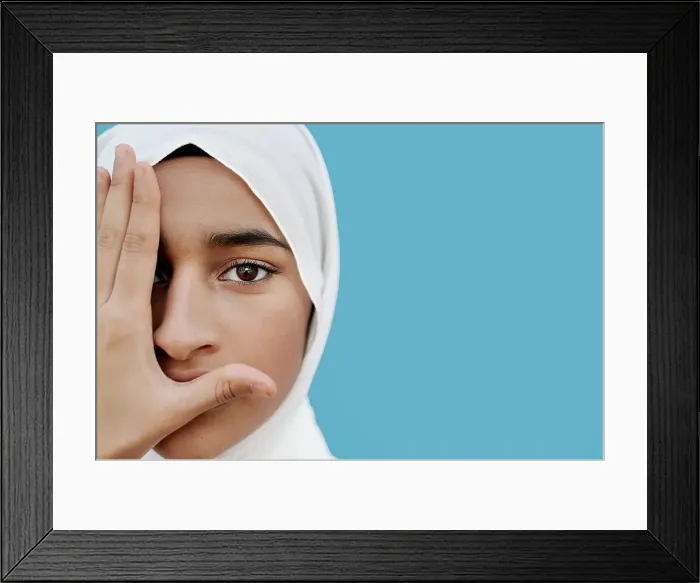 Framed Print : Muslim girl covering eye with hand against blue background