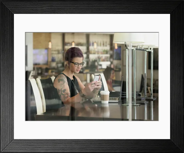Framed Print : Caucasian woman using cell phone and laptop in coffee shop Framed Print : Caucasian woman using cell phone and laptop in coffee shop