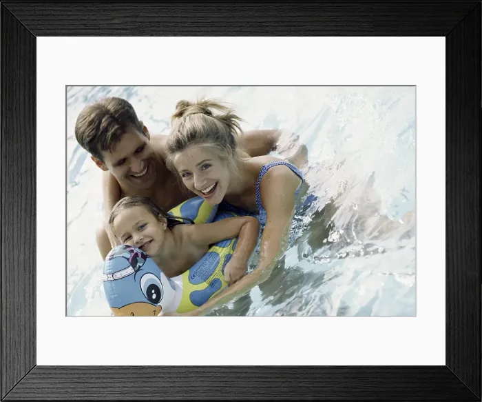 Framed Print : Portrait of a young couple playing in a swimming pool with their daughter