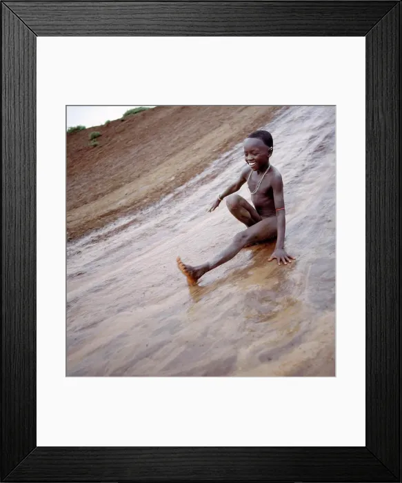 Framed Print : A young Samburu boy enjoys himself on a mudslide