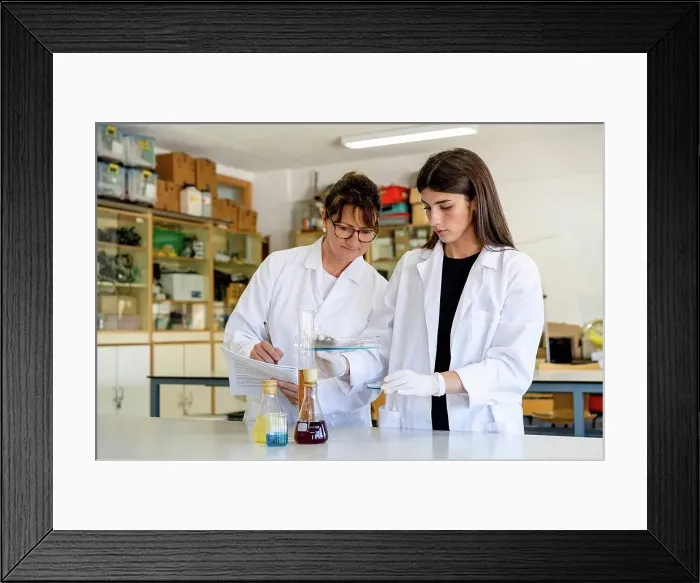 Framed Print : Mature female scientist with document examining chemical with colleague at laboratory Framed Print : Mature female scientist with document examining chemical with colleague at laboratory