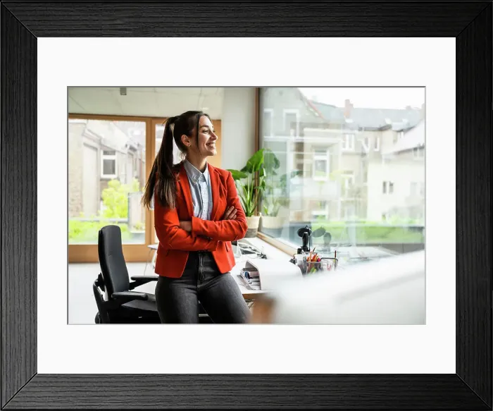 Framed Print : Smiling businesswoman with arms crossed looking through window in office Framed Print : Smiling businesswoman with arms crossed looking through window in office