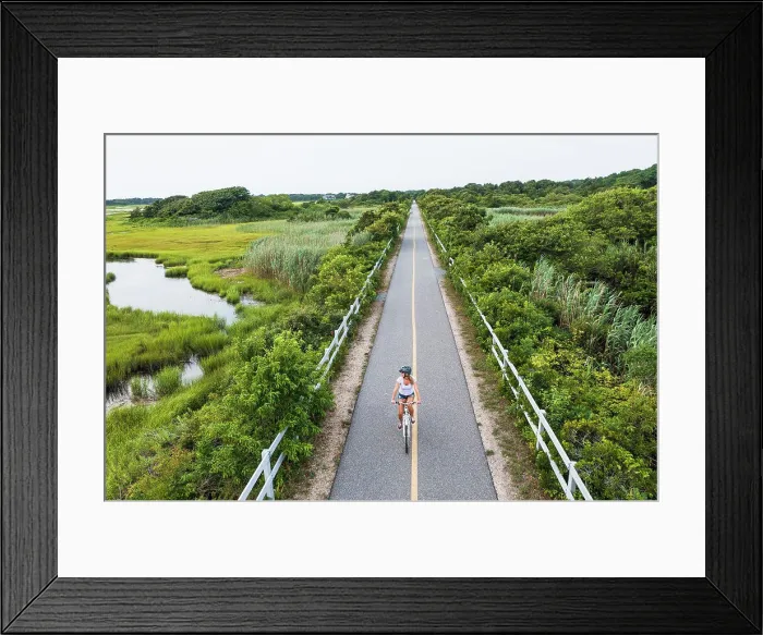 Framed Print : Aerial drone of Woman biking through Cape Cod Marshes bike path Framed Print : Aerial drone of Woman biking through Cape Cod Marshes bike path