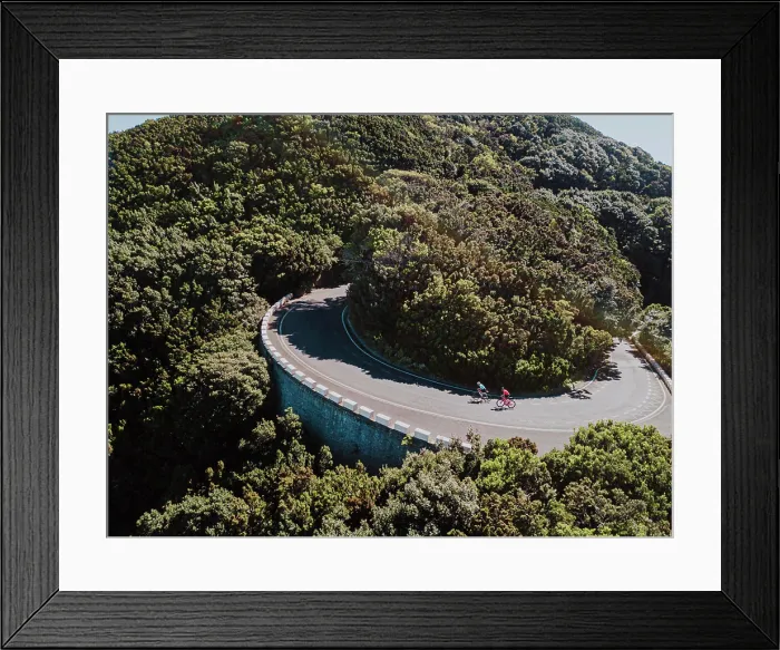 Framed Print : Aerial view of two cyclists on road bend in rain forest on sunny day