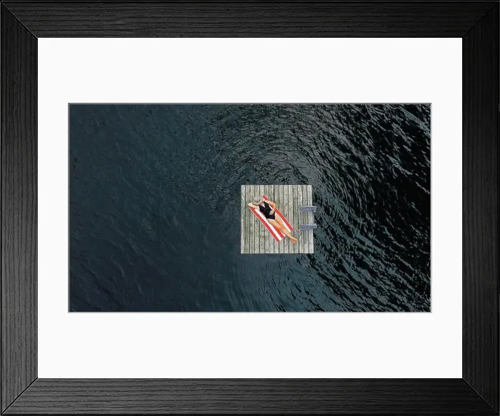 Framed Print : Aerial of woman relaxing alone on floating dock on lake in summer Framed Print : Aerial of woman relaxing alone on floating dock on lake in summer