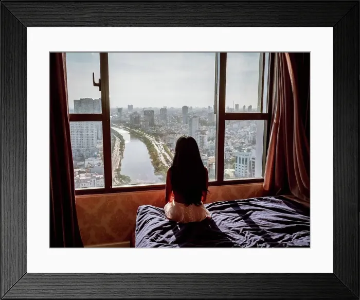 Framed Print : Rear view of an Asian woman sitting on a bed and looking through the window to the city of Ho Chi Minh, Vietnam Framed Print : Rear view of an Asian woman sitting on a bed and looking through the window to the city of Ho Chi Minh, Vietnam