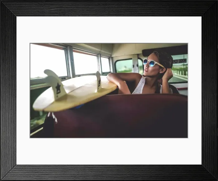 Framed Print : Young woman sitting on a bus with a surfboard