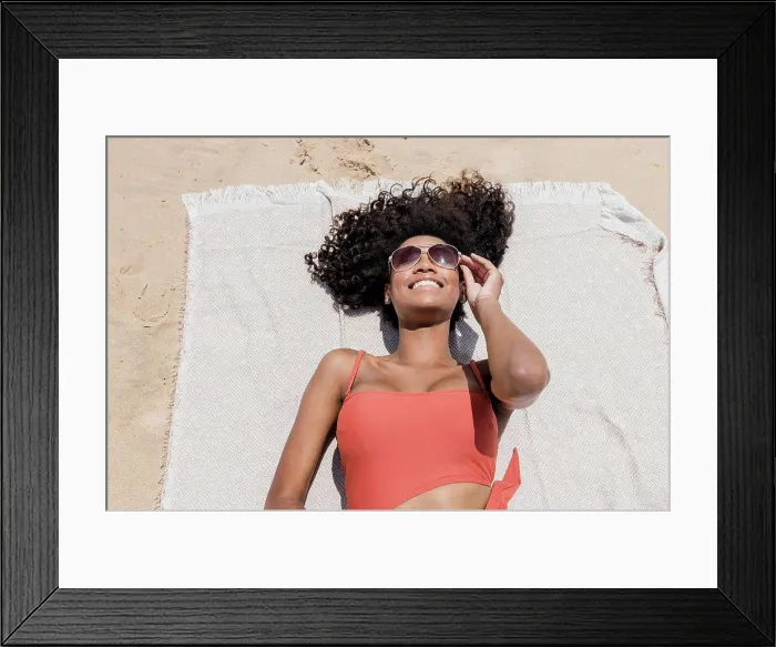 Framed Print : Smiling young woman with curly hair wearing sunglasses while lying on beach towel Framed Print : Smiling young woman with curly hair wearing sunglasses while lying on beach towel