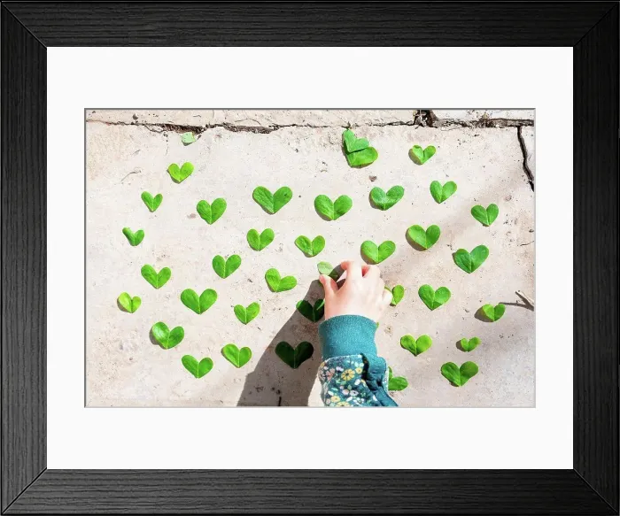 Framed Print : Girl arranging heart shaped green leaves pattern on cement Framed Print : Girl arranging heart shaped green leaves pattern on cement