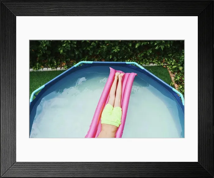Framed Print : Cenital view of part of a boy lying on a pink float resting in a pool Framed Print : Cenital view of part of a boy lying on a pink float resting in a pool