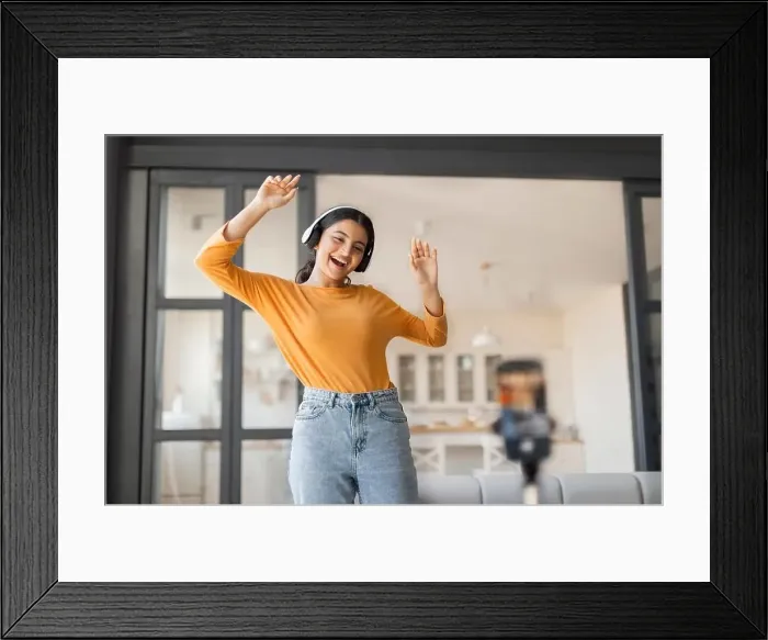 Framed Print : Cheerful young indian vlogger with headphones dancing joyfully while recording video Framed Print : Cheerful young indian vlogger with headphones dancing joyfully while recording video