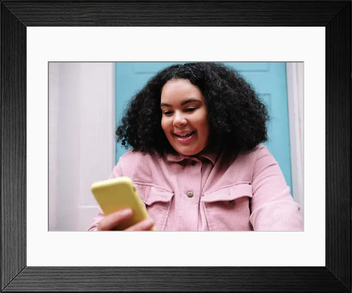 Framed Print : Happy young woman with curly hair surfing net through smart phone