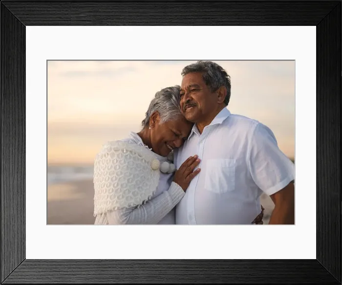 Framed Print : Smiling senior biracial woman embracing man looking away while standing at beach during sunset