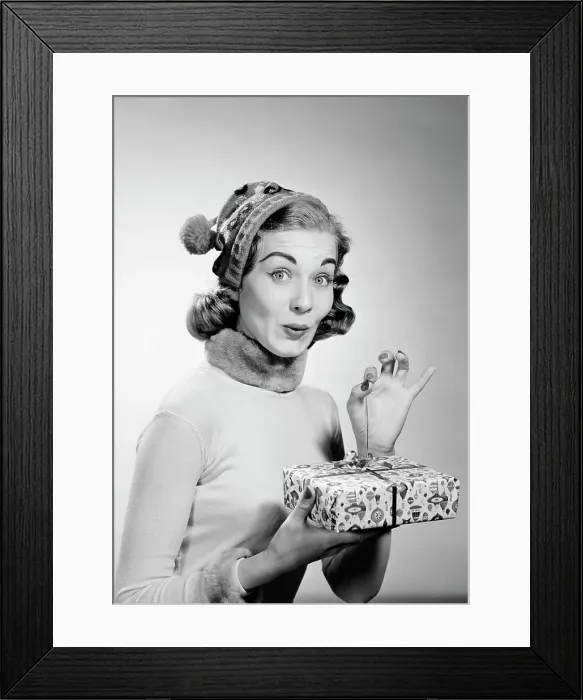 Framed Print : Young woman wearing knit hat opening christmas gift