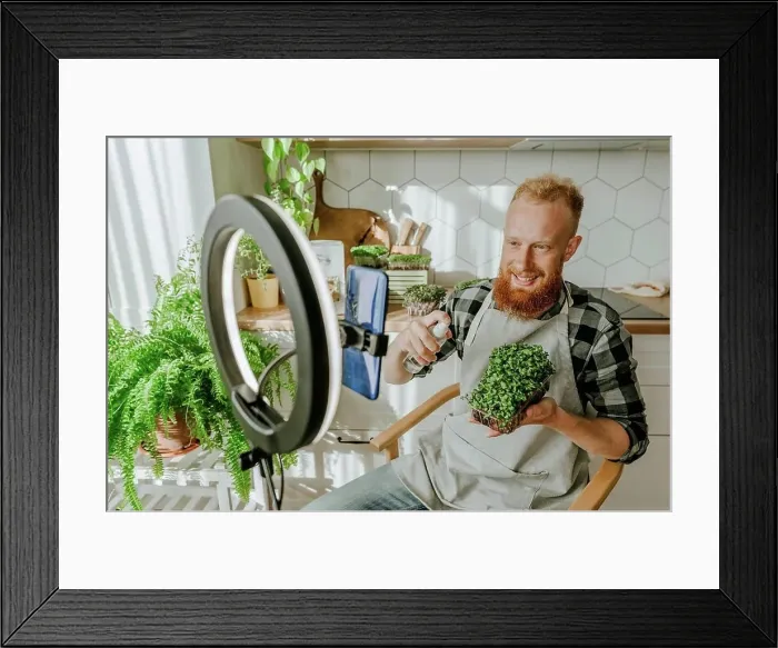 Framed Print : Smiling man spraying water on microgreens sitting in front of smart phone