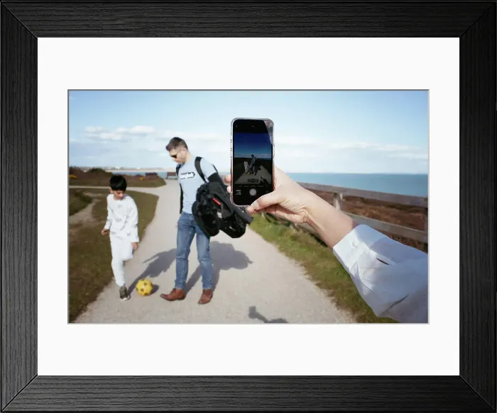 Framed Print : Woman taking pictures of her family playing football with her phone Framed Print : Woman taking pictures of her family playing football with her phone