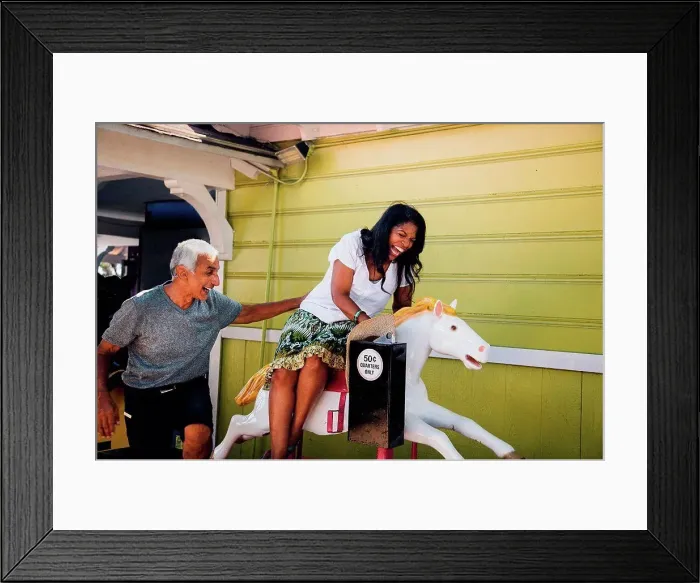 Framed Print : Senior woman on horse funfair ride, senior man standing beside her, laughing, Long Beach, California, USA