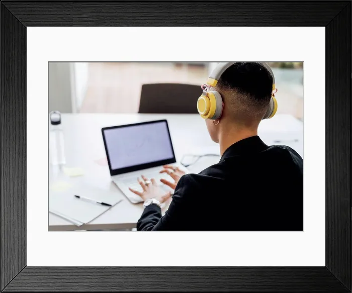 Framed Print : Female entrepreneur with headphones working on laptop in office Framed Print : Female entrepreneur with headphones working on laptop in office