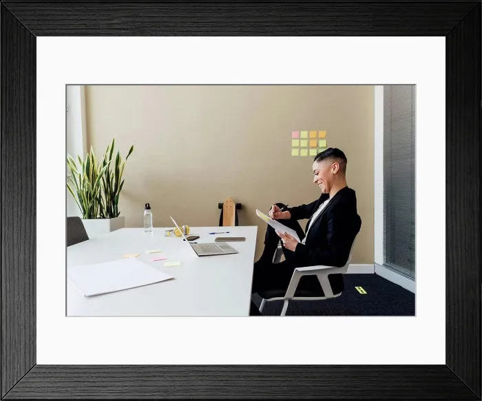 Framed Print : Smiling businesswoman writing on paper while sitting at desk in office Framed Print : Smiling businesswoman writing on paper while sitting at desk in office
