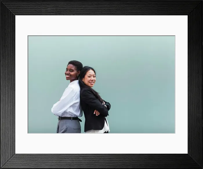 Framed Print : Smiling businesswomen with arms crossed standing back to back in front of blue wall Framed Print : Smiling businesswomen with arms crossed standing back to back in front of blue wall