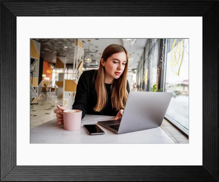 Framed Print : young girl in a cafe by the window working on a laptop Framed Print : young girl in a cafe by the window working on a laptop