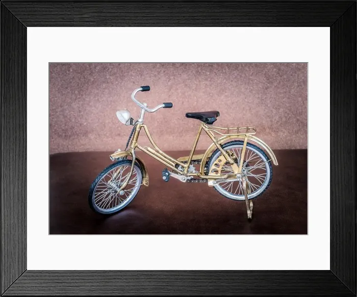 Framed Print : Small gold color toy bicycle on brown leather cushion Framed Print : Small gold color toy bicycle on brown leather cushion