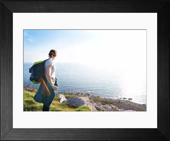 Framed Print : Hiker with backpack on cliff looking at view of ocean, Portland, UK Framed Print : Hiker with backpack on cliff looking at view of ocean, Portland, UK