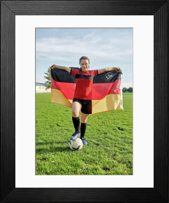 Framed Print : Happy girl standing with soccer ball and holding German flag on field Framed Print : Happy girl standing with soccer ball and holding German flag on field