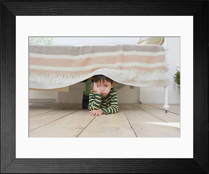 Framed Print : Boy hiding under a bed