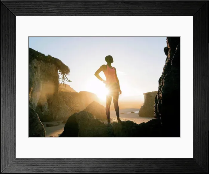 Framed Print : Young woman standing on rocks on beach, looking at view Framed Print : Young woman standing on rocks on beach, looking at view