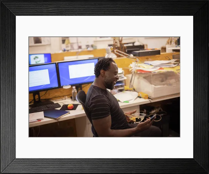 Framed Print : Smiling businessman eating lunch and using smart phone in office Framed Print : Smiling businessman eating lunch and using smart phone in office