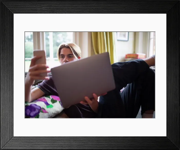Framed Print : Teenage boy using smart phone and laptop at home