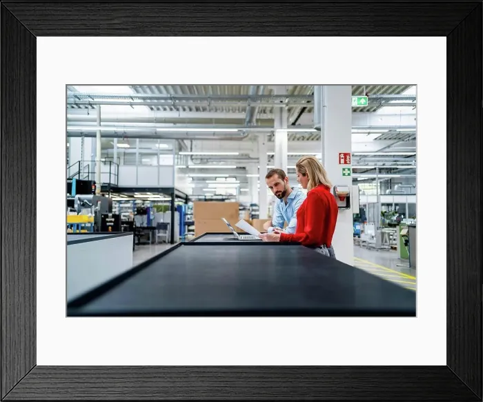 Framed Print : Business colleagues working on laptop at table in factory Framed Print : Business colleagues working on laptop at table in factory
