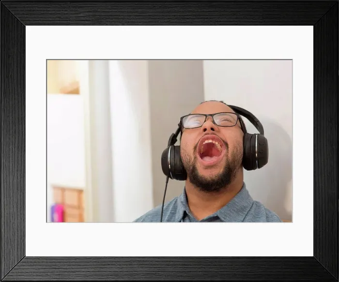 Framed Print : Happy African American man with Down Syndrome listening to music and singing with headphones at home Framed Print : Happy African American man with Down Syndrome listening to music and singing with headphones at home