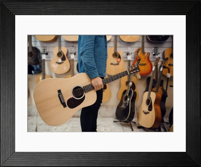 Framed Print : Young man holding acoustic guitar in music store. Assortment in musical instruments shop, male musician buying equipment