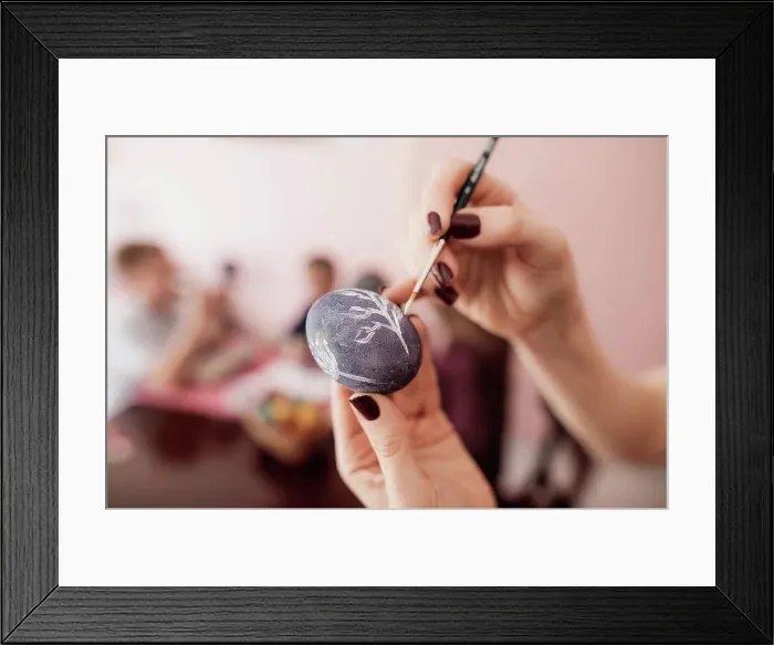 Framed Print : Woman painting Easter egg at home with children in background Framed Print : Woman painting Easter egg at home with children in background