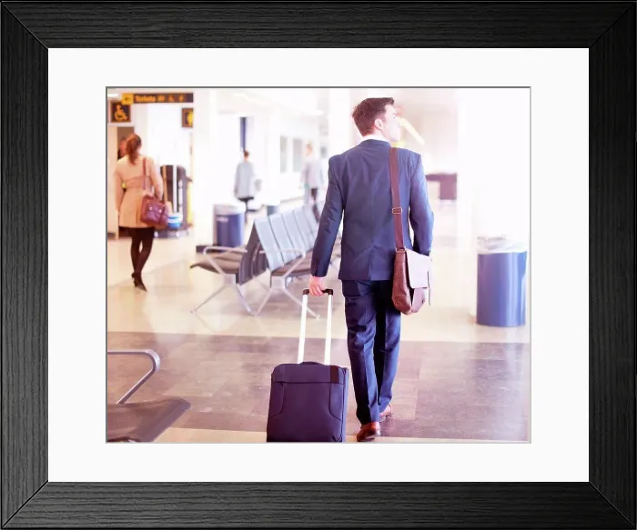 Framed Print : Businessman walking with wheeled suitcase in airport, rear view Framed Print : Businessman walking with wheeled suitcase in airport, rear view