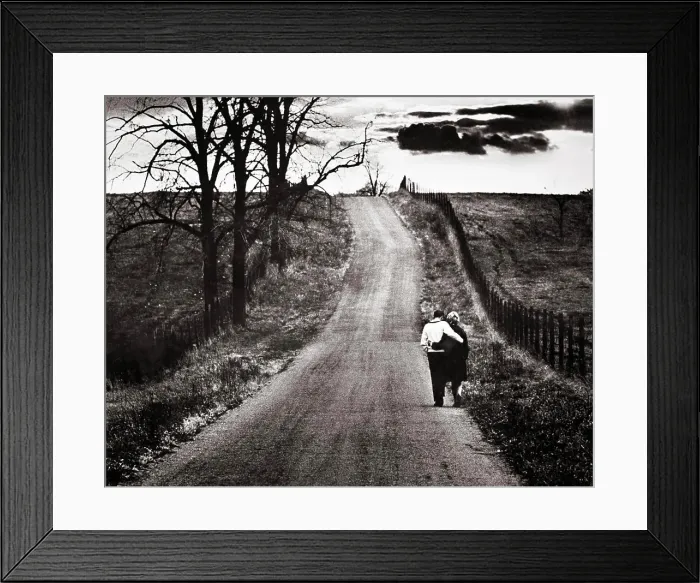 Framed Print : 1960s BACK VIEW MATURE COUPLE ARM IN ARM WALKING DOWN LONELY ROAD BARREN AUTUMN LANDSCAPE WITH OMINOUS CLOUDS ON
