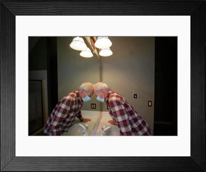 Framed Print : Senior man in Covid protective mask leaning head on mirror in bathroom