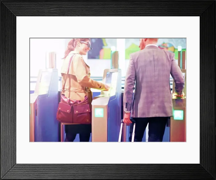 Framed Print : Businessman and woman walking through security gate at airport, rear view Framed Print : Businessman and woman walking through security gate at airport, rear view
