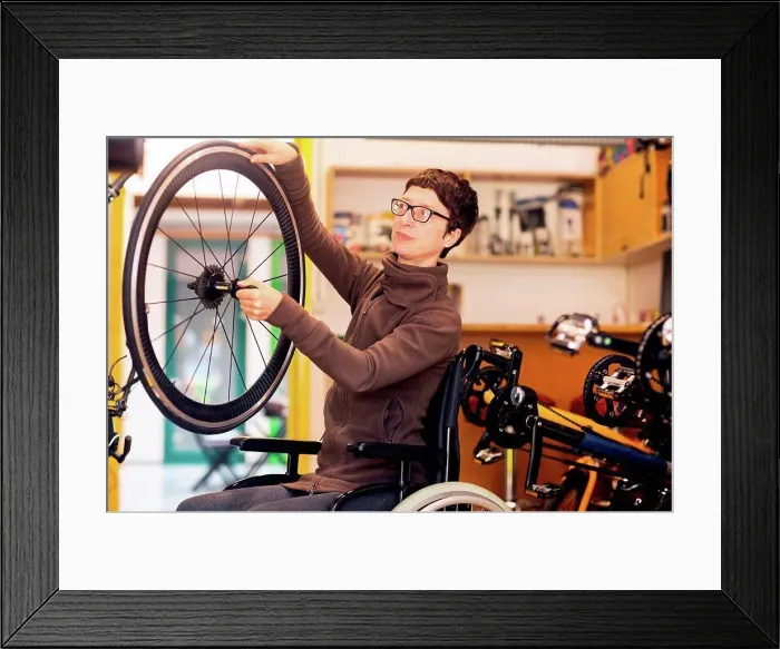 Framed Print : Woman in wheelchair in bicycle repair shop, holding bicycle wheel Framed Print : Woman in wheelchair in bicycle repair shop, holding bicycle wheel